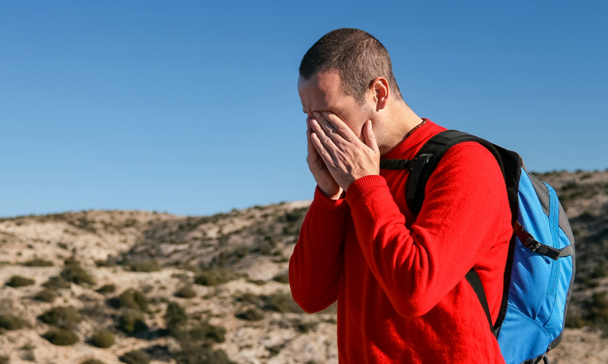 man wearing red crew-neck sweater with teal and black backpack outdoor during daytime